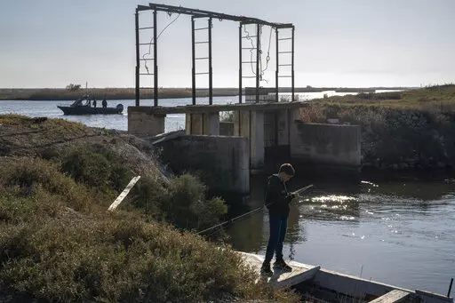 A boy fishes as police border guards on a boat patrol along the Evros River that forms a natural border between Greece and Turkey, on Sunday, Oct. 30, 2022. Greece is planning a major extension of a steel wall along its border with Turkey in 2023, a move that is being applauded by residents in the border area as well as voters more broadly.(AP Photo/Petros Giannakouris)