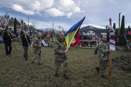 Ukrainian servicemen carry national flags and photos of their comrade Vasyl Boichuk who was killed in Mykolayiv in March 2022, during his funeral ceremony at the cemetery in Iltsi village, Ukraine, Tuesday, Dec. 26, 2023. (AP Photo/Evgeniy Maloletka)