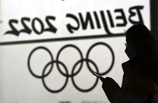 A woman looks at her phone as she passes an Olympic logo inside the main media center for the 2022 Winter Olympics, Jan. 18, 2022, in Beijing. (AP Photo/David J. Phillip, File)