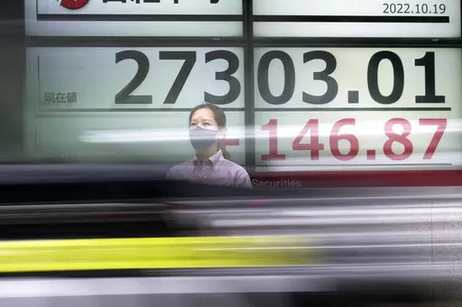 A person wearing a protective mask stands in front of an electronic stock board showing Japan's Nikkei 225 index as a vehicle passing by at a securities firm Wednesday, Oct. 19, 2022, in Tokyo. Asian stock markets were mixed Wednesday after Wall Street rose on strong corporate profit reports. (AP Photo/Eugene Hoshiko)