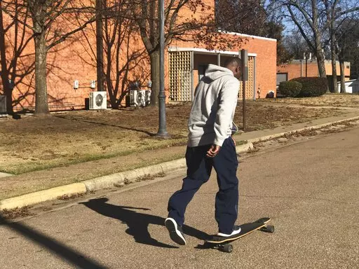 Mississippi University women's track and field coach Dedrick Burnett rides a skateboard on campus in Columbus, Miss., Wednesday, Dec. 8, 2021. o, Burnett is not the administrative assistant to Mississippi University for Women Athletic Director Jennifer Claybrook. But in an athletic department in which almost everybody wears many hats, Burnett’s hat rack is among the most crowded. (Tom Rysinski/The Commercial Dispatch via AP)