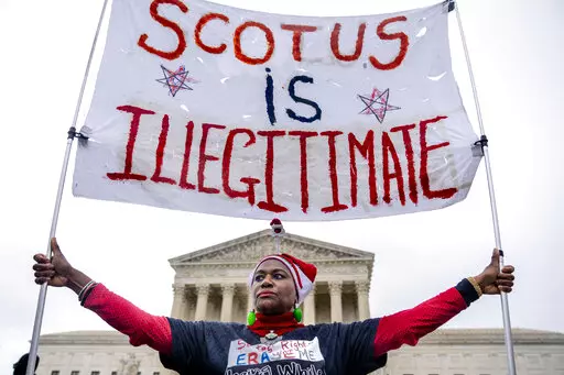 Nadine Seiler of Waldorf, Md., holds a sign that reads "SCOTUS is Illegitimate" in front of the Supreme Court in Washington, Wednesday, Dec. 7, 2022, as the Court hears arguments on a new elections case that could dramatically alter voting in 2024 and beyond. The case is from highly competitive North Carolina, where Republican efforts to draw congressional districts heavily in their favor were blocked by a Democratic majority on the state Supreme Court. (AP Photo/Andrew Harnik)