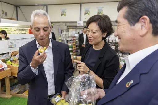 In this photo provided by U.S. Embassy, U.S. Ambassador to Japan Rahm Emanuel, left, eats a local fig at JA farmer’s market in Soma city, Fukushima prefecture, Thursday, Aug. 31, 2023. U.S. Ambassador Emanuel visited a northern Fukushima city Thursday and had seafood lunch with the mayor, talked to fishermen and stocked up on local produce at a grocery store to show they're all safe after the release of treated radioactive wastewater from the wrecked Fukushima Daiichi plant to the sea, backing