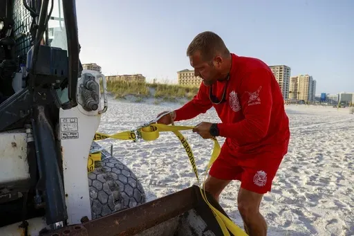 Patrick Brafford, a beach lifeguard manager, uses a tie down strap to help secure a compact track loader and a lifeguard tower to help pull it further away from the water in preparation of potential storm at Clearwater Beach on Saturday, Aug. 3, 2024, in Clearwater, Fla. (Jefferee Woo/Tampa Bay Times via AP)