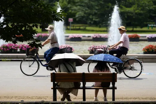 People holding parasols sit on the bench under an intense sun at a park in Tokyo, July 8, 2024. Japan’s total population marked the 15th straight year of decline, according to government data released Wednesday, July 24. (AP Photo/Eugene Hoshiko, File)