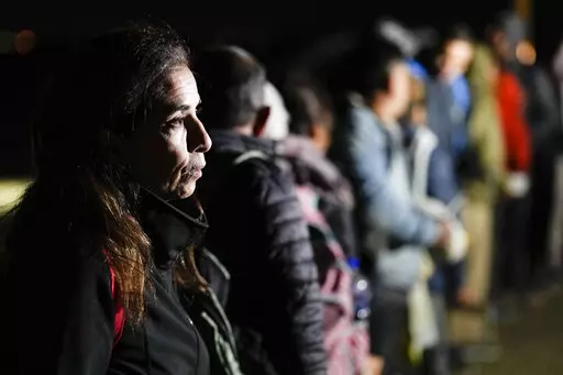 A woman from Cuba waits with other migrants to be processed to seek asylum after crossing the border into the United States, Friday, Jan. 6, 2023, near Yuma, Ariz. An underground market has emerged for migrants seeking U.S. sponsors since the Biden administration announced last month that it would accept a limited number of people from Venezuela, Cuba, Nicaragua and Haiti. Applicants for the humanitarian parole program need someone in the U.S. to promise to provide financial support for at least