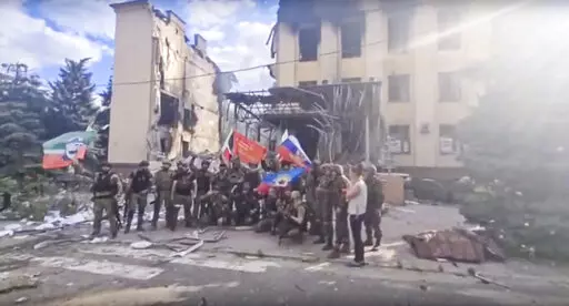 This photo taken from video provided by Ramzan Kadyrov's Official Telegram channel released on Saturday, July 2, 2022, shows Russian troops including soldiers of Chechen regiment waving Russian and Chechen republic national flags as they pose for a photo in front of a destroyed building in Lysychansk, Ukraine. After more than four months of ferocious fighting, Russia claimed full control over one of the two provinces in Ukraine’s eastern industrial heartland. (Ramzan Kadyrov's Official Telegra