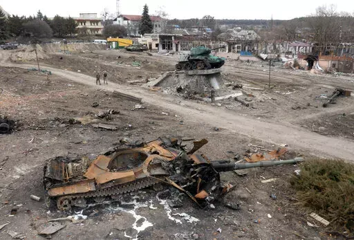 Local residents pass at a damaged Russian tank in the town of Trostsyanets, some 400km (250 miles) east of capital Kyiv, Ukraine, Monday, March 28, 2022. The monument to Second World War is seen in background. The more than month-old war has killed thousands and driven more than 10 million Ukrainians from their homes including almost 4 million from their country. (AP Photo/Efrem Lukatsky)