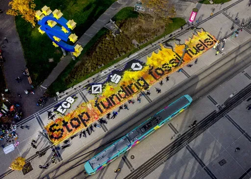 Climate activists lie after painting  "stop funding fossil fuels" on the square in front of the Euro sign in Frankfurt, during "Fridays for Future" event, Oct. 29, 2021. Insurance companies that have long said they'll cover anything, at the right price, are increasingly ruling out fossil fuel projects because of climate change — to cheers from environmental campaigners. (AP Photo/Michael Probst, File)