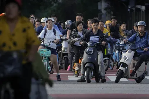 People on their bicycles and electric bikes wait at a traffic lights junction during the morning rush hour in Beijing, Friday, Sept. 13, 2024. (AP Photo/Andy Wong)