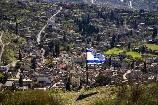 The Palestinian village of Burqa is seen as an Israeli flag is placed in the Jewish West Bank outpost of Homesh, Monday, Jan. 17, 2022. Palestinian residents of Burqa say the settlers' continued presence in Homesh, which was officially dismantled in 2005, makes it difficult to access their land and move safely in and out of their village. (AP Photo/Ariel Schalit)