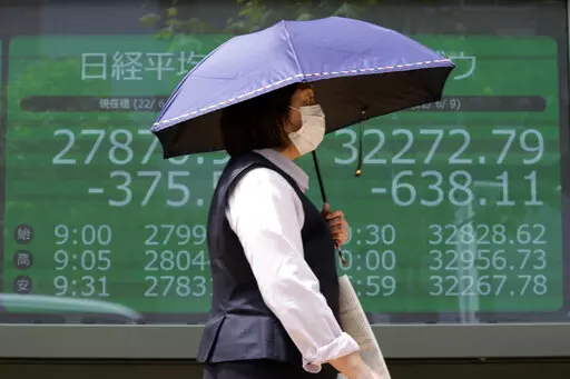 A woman wearing a protective mask in front of an electronic stock board showing Japan's Nikkei 225 and New York Dow indexes at a securities firm Friday, June 10, 2022, in Tokyo. Shares were mostly lower in Asia on Friday, with only Shanghai rising, after stocks tumbled on Wall Street on expectations central banks will focus on battling inflation with interest rate hikes. (AP Photo/Eugene Hoshiko)