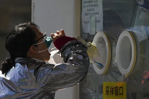 A woman pulls her face mask to get her routine COVID-19 throat swab at a coronavirus testing site in Beijing, Thursday, Oct. 6, 2022. Sprawling Xinjiang is the latest Chinese region to be hit with sweeping COVID-19 travel restrictions, as China further ratchets up control measures ahead of a key Communist Party congress later this month. (AP Photo/Andy Wong)