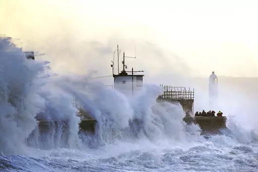 Waves crash against the sea wall and Porthcawl Lighthouse in Porthcawl, Bridgend, Wales, Britain, as Storm Eunice makes landfall Friday, Feb. 18, 2022. Millions of Britons are being urged to cancel travel plans and stay indoors Friday amid fears of high winds and flying debris as the second major storm this week prompted a rare “red” weather warning across southern England. ( Jacob King/PA via AP)