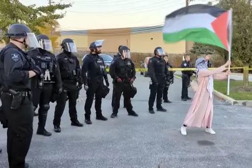 In this image taken from video, a demonstrator waves a Palestinian flag in front of a line of police officers during a pro-Palestinian demonstration Sunday, May 22, 2023, in Skokie, Ill. Cook County prosecutors have charged a 33-year-old man who pepper sprayed demonstrators Sunday at a pro-Palestinian protest near an Israel solidarity event in the Chicago suburbs with two felony hate crimes and two counts of aggravated battery. (AP Photo)