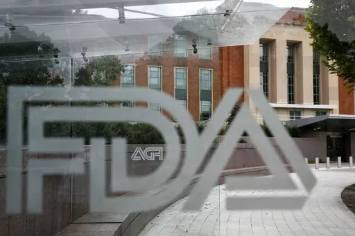 This Aug. 2, 2018 file photo shows the U.S. Food and Drug Administration building behind FDA logos at a bus stop on the agency's campus in Silver Spring, Md. The Food and Drug Administration has issued a negative review of a closely watched experimental drug for the debilitating illness known as Lou Gehrig’s disease. The review comes ahead of a meeting this week for outside experts to vote on the drug for ALS. The drug has been the focal point of a lobbying campaign by patients, their families