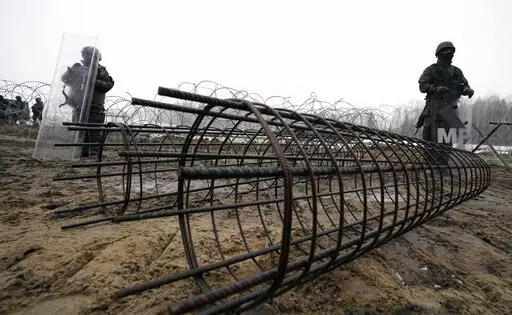 Guards and the military watching the start of work on the first part of a 180 kilometers (115 miles) and 5.5 meter (18ft)-high metal wall intended to block migrants from Belarus crossing illegally into EU territory, in Tolcze, near Kuznica, Poland, Jan. 27, 2022. When relations with Belarus deteriorated after its authoritarian President Alexander Lukashenko was declared the winner of an election widely seen as fraudulent, the government in Minsk sent thousands of migrants streaming across the EU