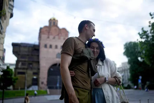 Stand-up comics Serhiy Lipko and Anastasia Zukhvala embrace during an interview with The Associated Press on their wedding day in Kyiv, Ukraine, Saturday, June 11, 2022. Lipko and Zukhvala are among those using humor as a weapon, and to keep spirits up. But he'll soon have a real weapon in his hands, because he's going into battle. (AP Photo/Natacha Pisarenko)