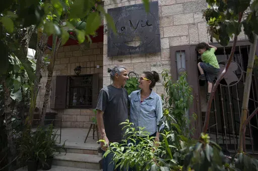 Kenae Totah, 5, right, plays while his parents Morgan Cooper, 41, center and Saleh Totah, right, pose for a photo in front of their restaurant, at the West Bank city of Ramallah, Monday, May 2, 2022.  The Israeli military body in charge of civilian affairs in the occupied West Bank has developed a new policy that would heavily regulate entry into the territory. Critics say it extends Israel's nearly 55-year military rule even further into every corner of Palestinian society. It would impose new 
