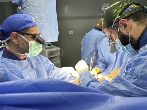 This handout photo taken on May 12, 2023 shows Dr. Adam Hamawy, left, a former U.S. Army combat plastic surgeon who volunteered in Gaza in May and Dr. Mohammed Tahir, a British surgeon, performing surgery on mangled hand from a blast injury at the European General Hospital, in Khan Younis, Gaza. (Adam Hamawy via AP)