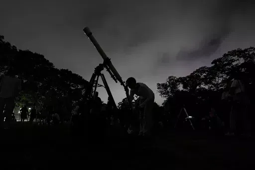 A girl looks at the moon through a telescope in Caracas, Venezuela, on Sunday, May 15, 2022. Six planets will line up in the early morning sky on June 3, 2024 but most won't be visible to the naked eye. A planetary parade happens relatively often when several planets align on the right side of the sun, making them visible across a narrow band of our sky. (AP Photo/Matias Delacroix)