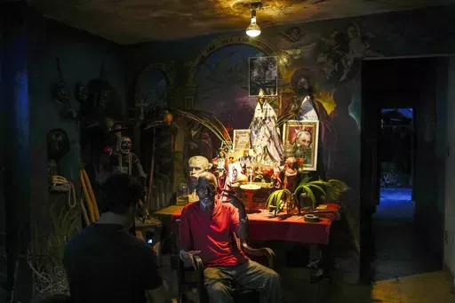Juan Gonzalez sits next to his altar adorned Santeria and Catholic deities along with a photo of the late Cuban leader Fidel Castro, at his home in El Cobre, Cuba, Feb. 10, 2024. Diverse beliefs can be found mixed together on altars in Cuban homes, with the Virgin Mary sharing space with a ceramic Buddha and a warrior spirit from the Afro-Cuban faith. (AP Photo/Ramon Espinosa, File)
