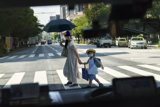 A pedestrian crossing a street with a child is seen through a taxi window in Tokyo, Monday, July 19, 2021. The number of babies born in Japan last year fell for an eighth straight year to a new low, government data showed Tuesday, Feb. 27, 2024, and a top official said it was critical for the country to reverse the trend in the coming half-dozen years. (AP Photo/David Goldman, File)
