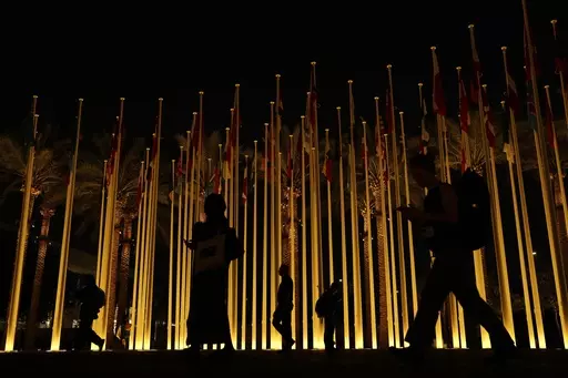 People walk near country's flags during the COP28 U.N. Climate Summit, Friday, Dec. 8, 2023, in Dubai, United Arab Emirates. (AP Photo/Rafiq Maqbool)