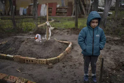 In the courtyard of their house, Vlad, 6, stands near the grave of his mother, who died, on the outskirts of Kyiv, Ukraine, Monday, April 4, 2022. Vlad's mother died last month when the family was forced to shelter in a basement during the occupation by the Russian army. The family still doesn't know what illness caused her death. (AP Photo/Rodrigo Abd)