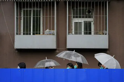 Residents holding umbrellas line up in the rain along the barricaded fence for COVID tests outside the locked-down apartment building on Wednesday, April 27, 2022, in Beijing. China employs a variety of metal barricades, metal sheeting and door locks to keep people inside their apartments, buildings or complexes during lockdowns. The barriers have been deployed in multiple cities across China as part of the fight against COVID-19. (AP Photo/Andy Wong)