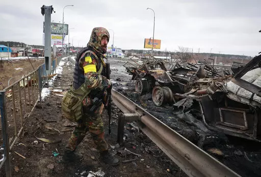 An armed man stands by the remains of a Russian military vehicle in Bucha, close to the capital Kyiv, Ukraine, March 1, 2022.  (AP Photo/Serhii Nuzhnenko, File)