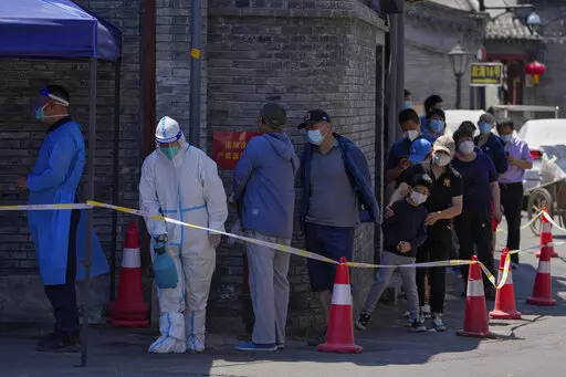 A worker in protective suit sprays disinfectant as residents line up for mass COVID test on Monday, May 16, 2022, in Beijing. Authorities say most of Shanghai has stopped the spread of the coronavirus in the community and fewer than 1 million people remain under strict lockdown. China's largest city is moving toward reopening as economic data showed the gloomy impact of China's "zero-COVID" policy. (AP Photo/Andy Wong)