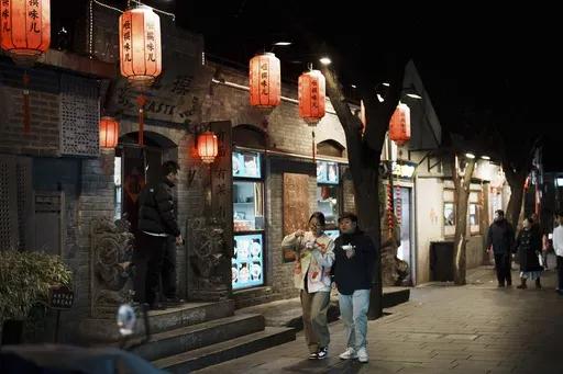 Shoppers walk at a tourist attraction area, Nanluogu Alley in the evening in downtown Beijing, China, Saturday, March 8, 2025. (AP Photo/Vincent Thian)
