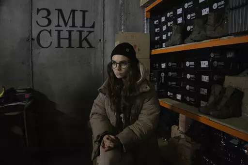 Co-founder Kseniia Drahaniuk of the nonprofit group Zemliachky pauses during an interview in front of shelves stacked with military boots at its supply room in Kyiv, Ukraine, on Tuesday, Dec. 6, 2022. The home-grown association helps equip women soldiers who have joined Ukraine's army by the thousands in response to Russia's invasion nearly 10 months ago. (AP Photo/Vasilisa Stepanenko)