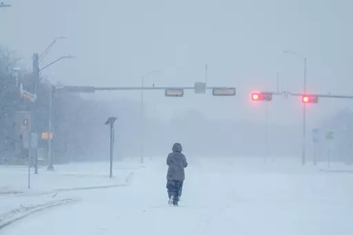 A jogger trots on a snow-covered road during a winter storm, Jan. 15, 2024, in Grand Prairie, Texas. Winter weather brings various hazards that people have to contend with to keep warm and safe. These dangers can include carbon monoxide poisoning, hypothermia and frozen pipes that can burst and make homes unlivable. Public safety officials and experts say there are multiple ways people can prepare themselves to avoid these hazards and keep themselves safe. (AP Photo/Julio Cortez, file)