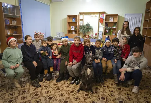 Children traumatized by the war pose for photo with an American Pit Bull Terrier "Bice" in the Center for Social and Psychological Rehabilitation in Boyarka close Kyiv, Ukraine, Wednesday, Dec. 7, 2022. Bice is an American pit bull terrier with an important and sensitive job in Ukraine — comforting children traumatized by the war. The Center for Social and Psychological Rehabilitation is a state-operated community center where a group of people are trying to help those who have experienced a t