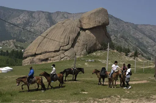 Tourists enjoy horseback riding near the iconic Turtle Rock outcrop at the Terejl National Park outside Ulaanbaatar, Mongolia on July 3, 2024. (AP Photo/Ng Han Guan)