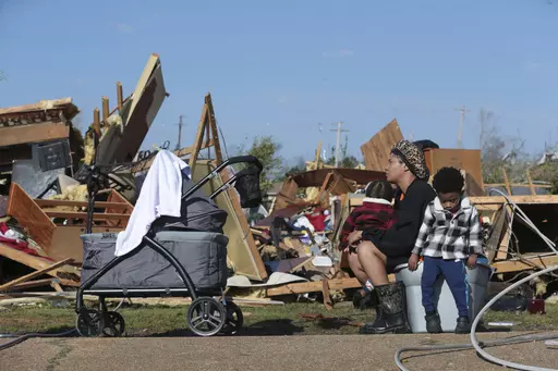 Melanie Childs of Amory, Miss., sits on a bucket and holds her two children, Mila, 1, left, and Major, 2, as they view whats left of her grandfather, Barrie Young, home Saturday 25, 2023. Emergency officials in Mississippi say several people have been killed by tornadoes that tore through the state on Friday night, destroying buildings and knocking out power as severe weather produced hail the size of golf balls moved through several southern states. (Thomas Wells/The Northeast Mississippi Daily