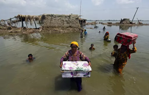 Women carry belongings salvaged from their flooded home after monsoon rains, in the Qambar Shahdadkot district of Sindh Province, of Pakistan, Sept. 6, 2022. From drought to floods and sea level rise, the cost of damage caused by climate change will only get higher as the world warms, sparking concerns from both top officials and activists about how to pay for it. (AP Photo/Fareed Khan, File)