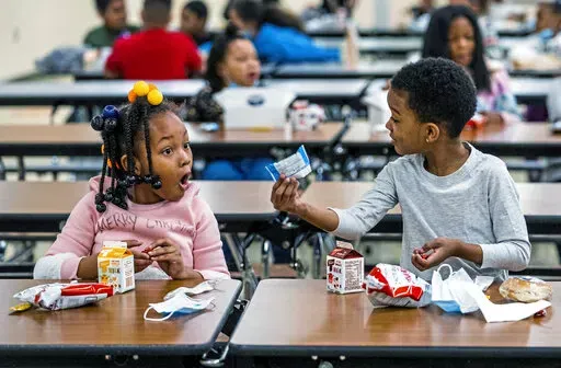 First graders, from left, Kendal Kates and Ryan Kenney are excited about the contents of their boxed lunches at Langley K-8 School, Dec. 23, 2021, in the Sheraden neighborhood in Pittsburgh. The Biden administration has issued transitional standards for school lunches that are meant to get cafeterias back on a healthier course as they recover from pandemic and supply chain disruptions.  The “bridge” rule announced by the U.S. Agriculture Department on Friday extends emergency flexibilities f