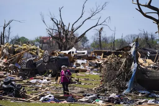 A woman walks near an uprooted tree, a flipped vehicle and debris from homes damaged by a tornado, March 27, 2023, in Rolling Fork, Miss. While the dangers of tornadoes to mobile homes have long been known, and there are ways to mitigate the risk, the percentage of total tornado deaths that happen in mobile homes has been increasing. (AP Photo/Julio Cortez, File)
