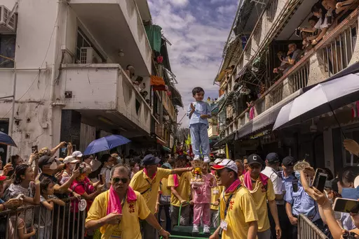 A child is hoisted up as participants take part in the Piu Sik Parade at the Bun Festival in Cheung Chau Island in Hong Kong, Friday, May 26, 2023. (AP Photo/Louise Delmotte)