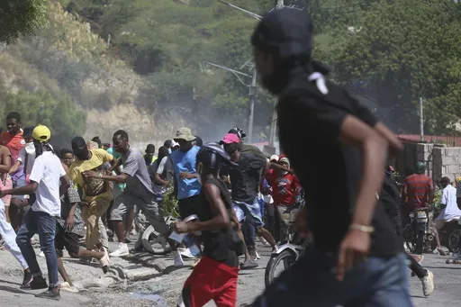 People run from tear gas fired by police to disperse protesters demanding police and the Prime Minister take immediate action against gangs in Port-au-Prince, Haiti, Monday, Aug. 19, 2024. (AP Photo/Odelyn Joseph)