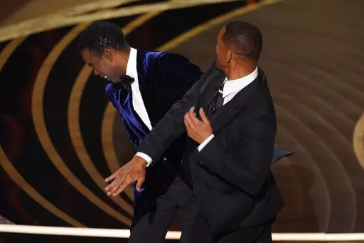 Will Smith, right, hits presenter Chris Rock on stage while presenting the award for best documentary feature at the Oscars on Sunday, March 27, 2022, at the Dolby Theatre in Los Angeles. Rock will be the first artist to perform on Netflix's first-ever live, global streaming event. (AP Photo/Chris Pizzello, File)