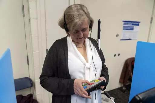 Patti Chang, who is blind, uses headphones and audio along with an electronic controller outfitted with braille to vote in the Chicago mayoral runoff election at the Roden Branch of the Chicago Public Library Wednesday, March 22, 2023, in Chicago. Like many voters with disabilities, Chang faces barriers at the polls most voters never even consider — missing ramps or door knobs, for example. The lack of help or empathy from some poll workers just adds to the burden for people with disabilities.