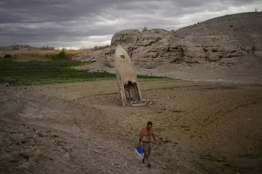 A man walks by a formerly sunken boat standing upright into the air with its stern buried in the mud along the shoreline of Lake Mead amid a drought at the Lake Mead National Recreation Area near Boulder City, Nev., June 22, 2022. Costly weather disasters kept raining down on America last year, pounding the nation with 18 climate extremes that caused at least $1 billion in damage each, totaling more than $165 billion, federal climate scientists calculated Tuesday, Jan. 10, 2023. (AP Photo/John L
