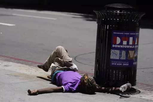 A homeless person lies on the sidewalk while holding a water bottle, Sunday, July 2, 2023, in downtown Los Angeles. Excessive heat warnings remain in place in many areas across the U.S. and are expected to last at least through Monday. (AP Photo/Damian Dovarganes)