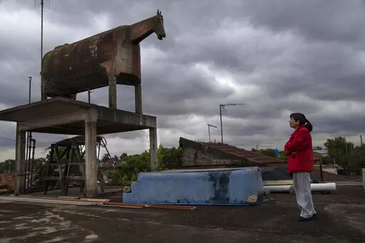 Liliana Gutiérrez looks at the horse-shaped water tank built by her father in the San Jorge neighborhood of Florencio Varela, Argentina, Monday, Oct. 26, 2022. Nostalgia led Gervasio Gutiérrez, a peasant turned bricklayer from the distant province of Jujuy, to build the tank on the terrace of his daughter's house. Before the existence of GPS trackers, the horse-shaped water tank that many confused with a cow, was often used as a reference point for travelers. (AP Photo/Rodrigo Abd)