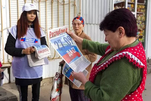 A volunteer of Luhansk regional election commission distributes newspapers to local citizens prior to a referendum in Luhansk, Luhansk People's Republic controlled by Russia-backed separatists, eastern Ukraine, Thursday, Sept. 22, 2022. Authorities in Russian-controlled regions in eastern and southern Ukraine are preparing to hold referendums on becoming part of Russia — a move that could allow Moscow to escalate the war. The votes start Friday in the Luhansk, Kherson and partly Russian-contro