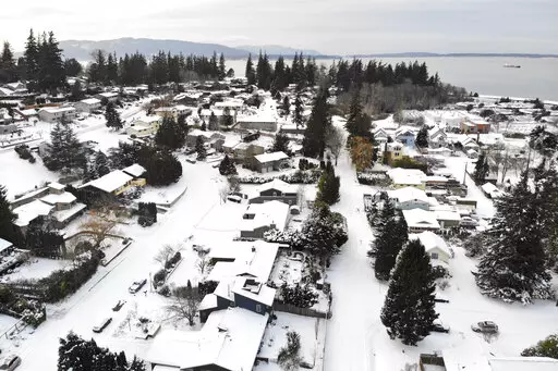 In this photo taken from a drone, snow covers streets, sidewalks and homes where nearly a foot of snow fell over the weekend, Monday, Dec. 27, 2021, in a neighborhood near Bellingham Bay in Bellingham, Wash. Emergency warming shelters were opened throughout western Washington and Oregon as temperatures plunged into the teens and forecasters said an arctic blast would last for several days. (AP Photo/Elaine Thompson)